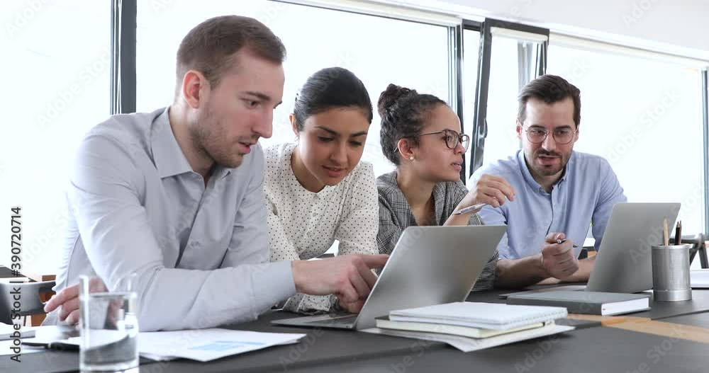 Focused young caucasian employee sharing good project results in computer application with smiling indian colleague. Busy diverse multiethnic business people involved in working processes at office.