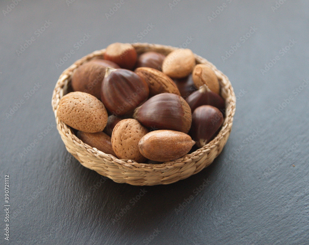Mixed nuts - almond, chestnut, pecan, hazelnut, sweet chesnut (castanea sativa ), Spanish Chestnut, woven rustic bucket on dark grey stone background Mixed nuts - almond, chestnut, pecan, hazelnut, sweet chesnut (castanea sativa ), Spanish Chestnut, woven rustic bucket on dark grey stone background