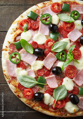 Pizza with ham, mozzarella cheese, cherry tomatoes, green and jalapeno pepper, black olives and fresh basil. Dark wooden background. Top view.	