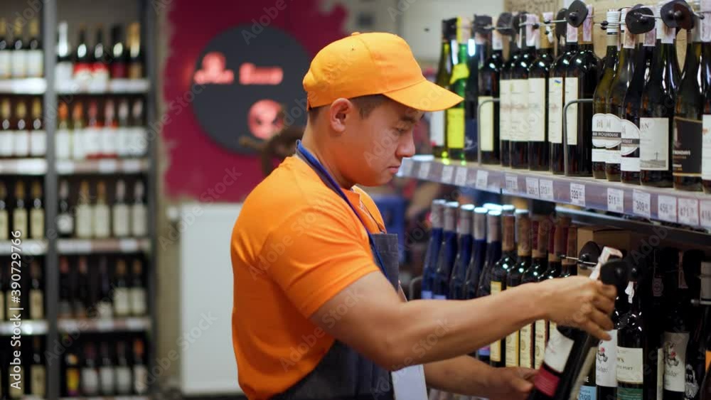 Korean supermarket worker in orange uniform sorting and arranging alcohol beverage bottles into sections working busy at grocery store. Alcohol section. People, jobs and occupation.