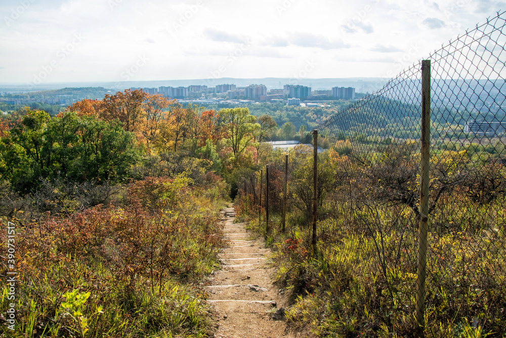 Pedestrian path along an old fence in an autumn landscape with the city in the background