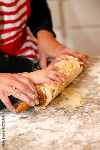 Toddler girl in red apron baking chocolate chip christmas cookies at holidays with grandma in kitchen - close up of hands with rolling pin
