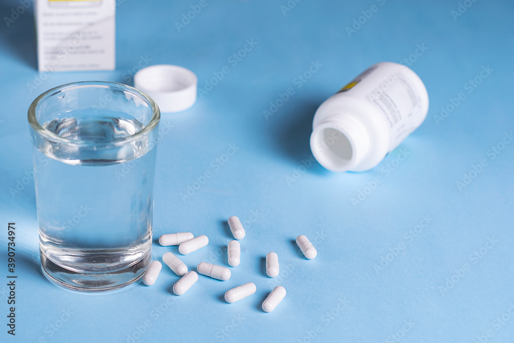 A bunch of vitamins and nutritional supplements with a glass of water in a blue background A bunch of vitamins and nutritional supplements with a glass of water in a blue background