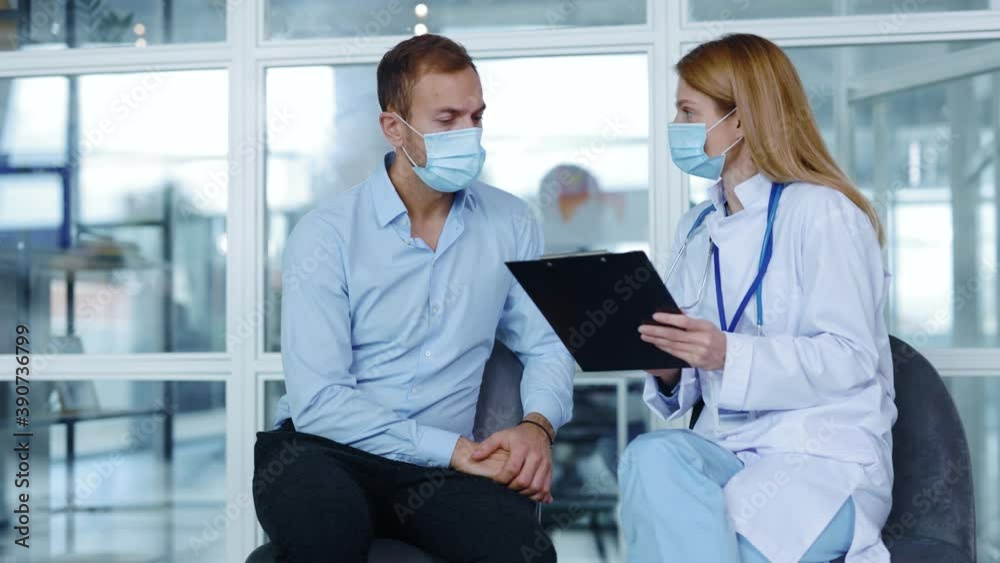 In hospital corridor man with medical mask sitting speaking with woman doctor about diagnosis during consultation. Patient clinic covid coronavirus illness. Slow motion In hospital corridor man with medical mask sitting speaking with woman doctor about diagnosis during consultation. Patient clinic covid coronavirus illness. Slow motion