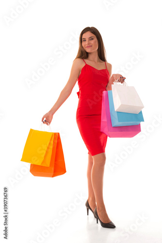 Brunette smiling while standing with purchases on white background. Girl posing at camera with packages after shopping. 