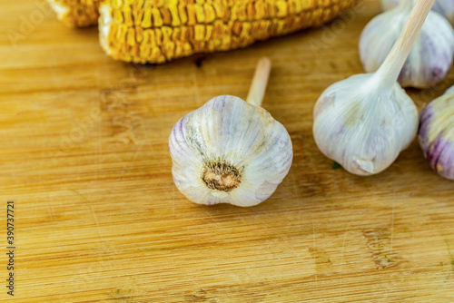 three heads of dried white garlic lies on a wooden table on a background of corn