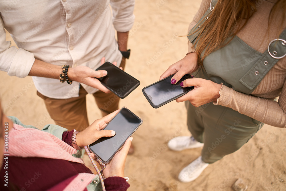 Group of three young people using smartphones together.