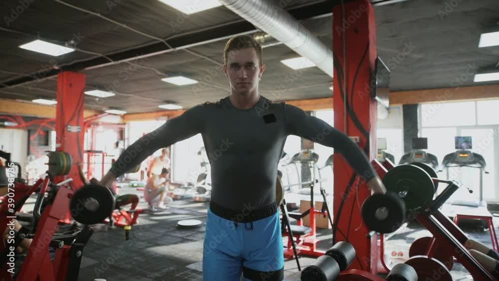 Handsome athletic man performing Side raise exercise with dumbbells at gym Handsome athletic man performing Side raise exercise with dumbbells at gym
