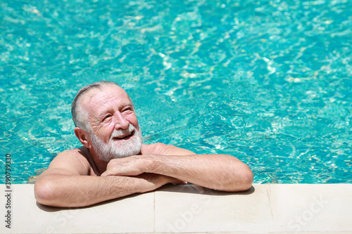 Senior fit active caucasian man with white beardstanding and looking away after swimming in water of swimming pool outdoor, happy and enjoying healthy lifestyle deserved retirement during holiday