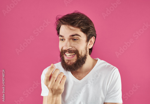 Happy young man on a pink background in a white T-shirt and a thick beard gesticulate with his hands