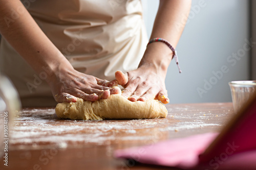 Hands of a young woman, kneading dough to make bread on top of a wooden table