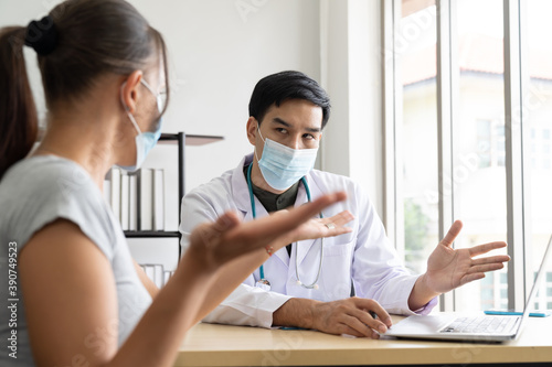 Woman wearing face mask sitting and talking to the professional psychologist while wearing face mask conducting a consultation and using computer notebook during coronavirus or COVID 19 outbreak