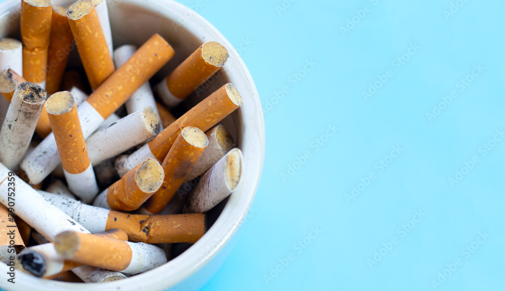 Cigarettes buds in a transparent ashtray on blue background. Cigarettes buds in a transparent ashtray on blue background.