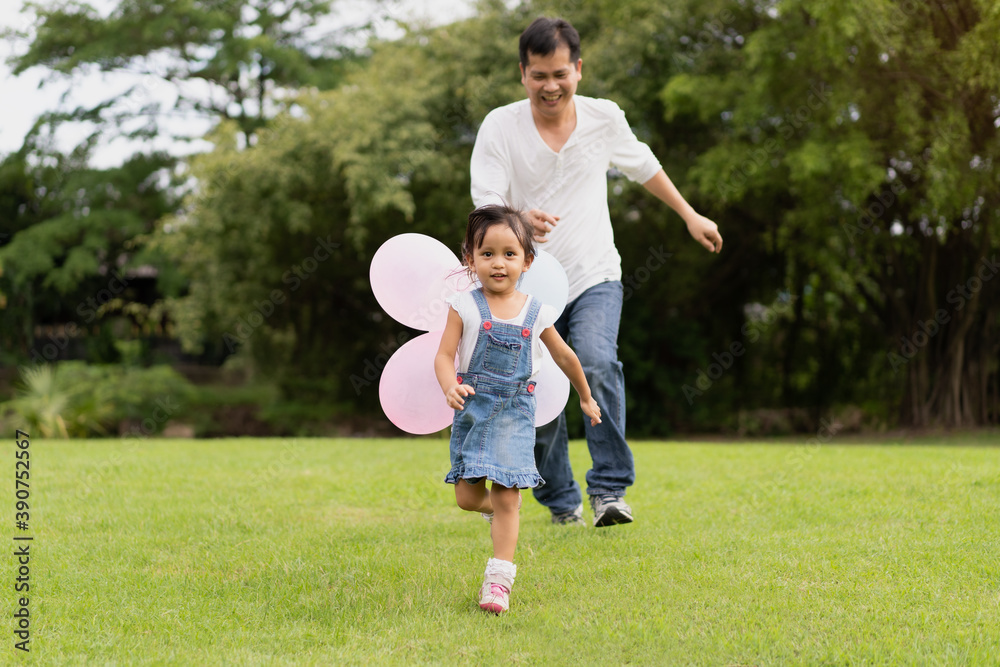 Fototapeta premium Asian father and daughter are playing the balloons and they running and laughing together with fully happy moment in the park, concept of outdoor activity in family lifestyle.