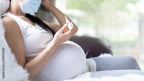Unidentified pregnant woman is checking body temperature for symptom of fever, headache of viral infection, concept of sickness and healthcare in pregnancy in the situation of covid 19 outbreak.