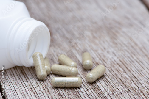 Green natural herbal powder capsules in white bottle on wood