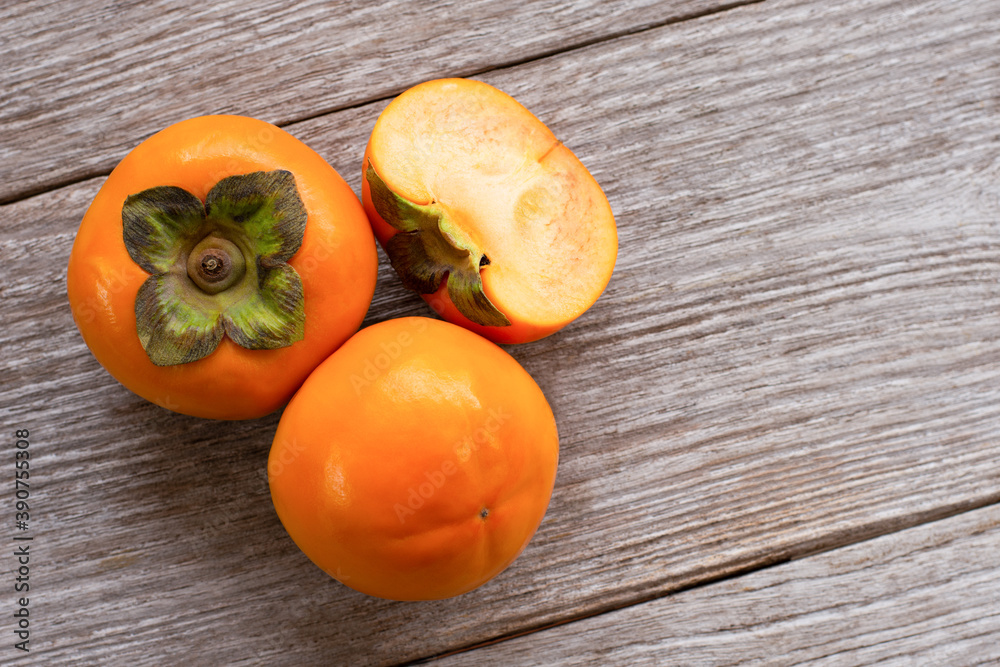 Fresh orange organic ripe Fuyu Persimmons or Persimon fruits with slice isolated on wood table Fresh orange organic ripe Fuyu Persimmons or Persimon fruits with slice isolated on wood table
