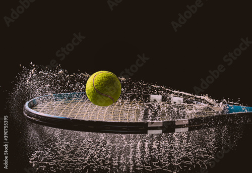 Closeup shot of a tennis ball and racket with a splash of water isolated on a dark background