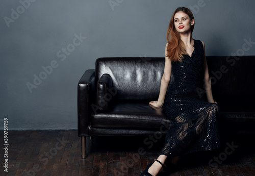 Elegant woman in evening black dress on a leather sofa indoors