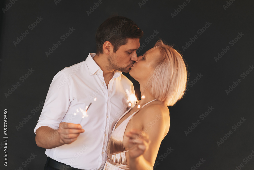 Beautiful happy couple young family kissing in evening dresses with sparkler on the dark background, selective focus Beautiful happy couple young family kissing in evening dresses with sparkler on the dark background, selective focus