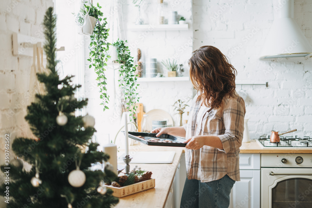 Attractive smiling woman with curly hair in plaid shirt bakes cookies at bright kitchen at the home Attractive smiling woman with curly hair in plaid shirt bakes cookies at bright kitchen at the home