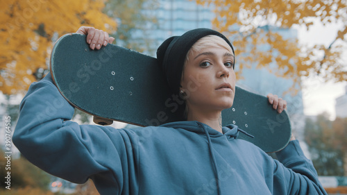 Young caucasian confident woman skater holding skateboard behind her head in the park in autumn. High quality photo photo