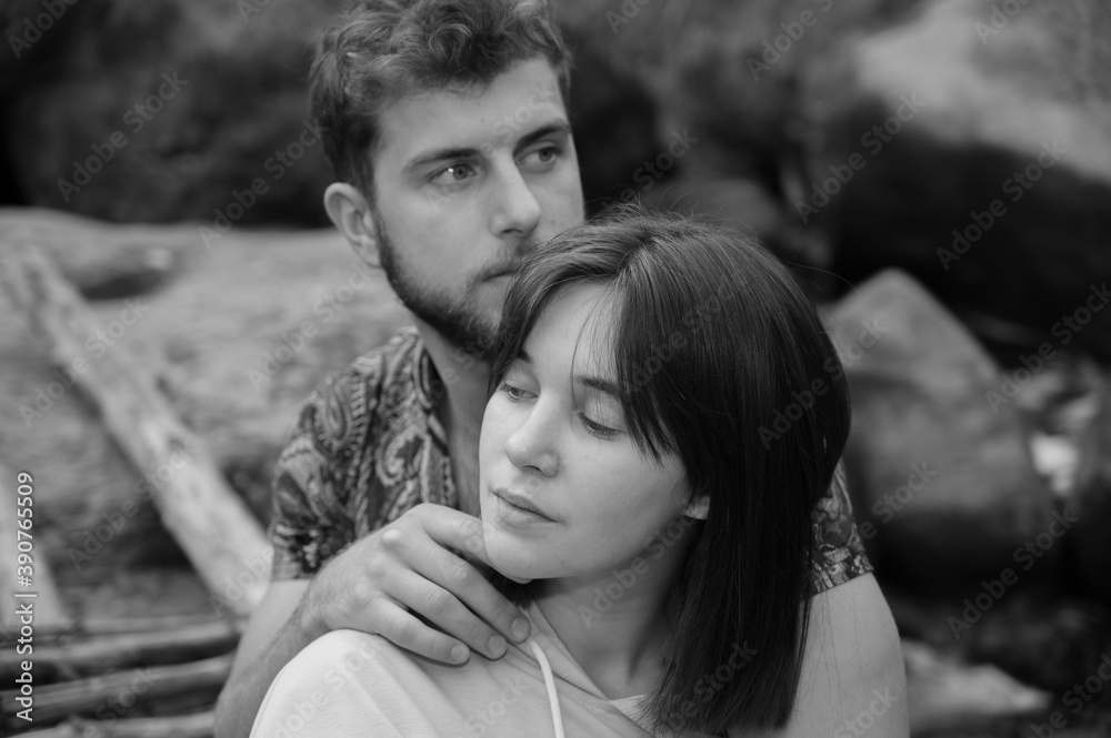 Serious couple sit on wooden footbridge between rocks over stream. Boyfriend flirts with girlfriend, she pretends to ignore. Happiness in relationships. Beautiful natural black and white matte tones. Serious couple sit on wooden footbridge between rocks over stream. Boyfriend flirts with girlfriend, she pretends to ignore. Happiness in relationships. Beautiful natural black and white matte tones.