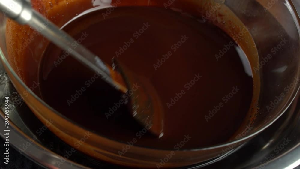 Close-up of dark chocolate. Tempering dark chocolate. Chocolate in a glass container is cooled with ice. Chocolatier makes handmade chocolate. Close-up of dark chocolate. Tempering dark chocolate. Chocolate in a glass container is cooled with ice. Chocolatier makes handmade chocolate.