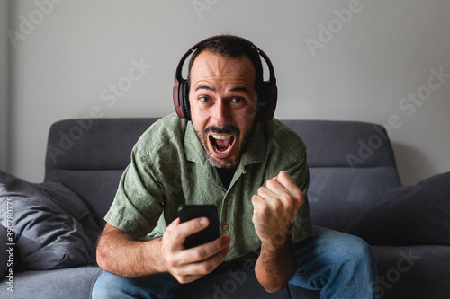 man sitting on sofa and shouting for joy, while winning sports betting with mobile phone  photo