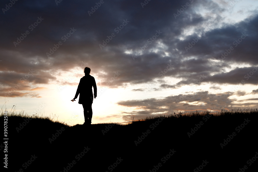 silhouette of a girl standing with a flower in her hands on a background of sunset