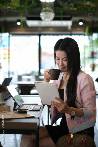 Portrait of businesswoman reading information in notebook while drinking coffee at meeting room.