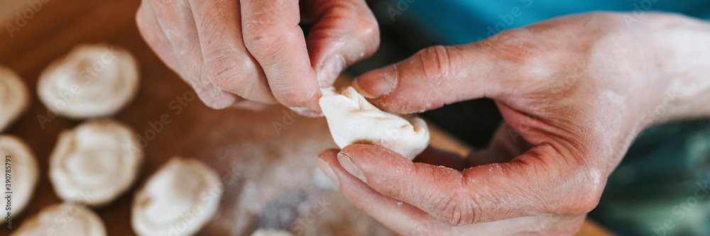 hands of senior man cooking and molding small homemade uncooked dumplings with meat on kitchen table. national traditional Russian cuisine. do it yourself. top view. banner hands of senior man cooking and molding small homemade uncooked dumplings with meat on kitchen table. national traditional Russian cuisine. do it yourself. top view. banner