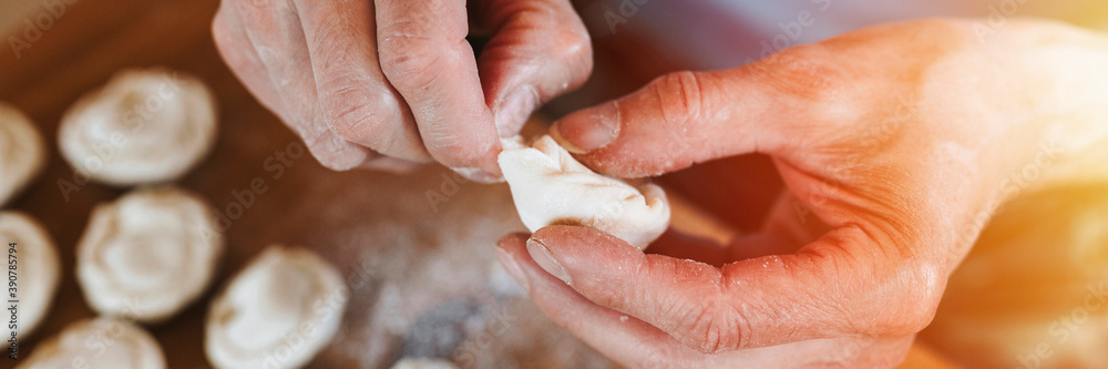 hands of senior man cooking and molding small homemade uncooked dumplings with meat on kitchen table. national traditional Russian cuisine. do it yourself. top view. banner. flare hands of senior man cooking and molding small homemade uncooked dumplings with meat on kitchen table. national traditional Russian cuisine. do it yourself. top view. banner. flare