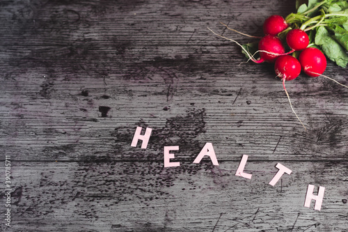 Beautiful and elegant dark background with striking pink HEALTH letters with bunches of radishes on one side, where there is space to write a small text