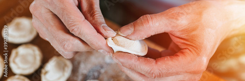 hands of senior man cooking and molding small homemade uncooked dumplings with meat on kitchen table. national traditional Russian cuisine. do it yourself. top view. banner. flare