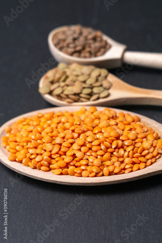 various types of dry lentils in wooden spoons on a dark background. vertical photo, selective focus