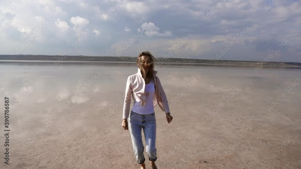 Beatiful girl by the lake on the shore, running and walking on shore, making fun