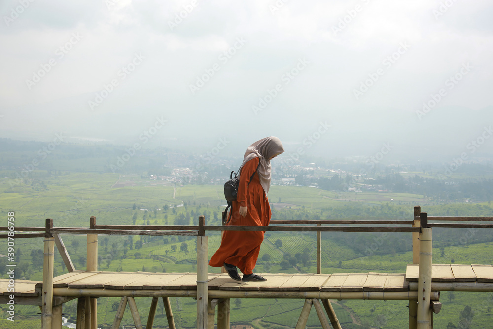 Moslem woman traveler walking on wooden bridge above the misty tea plantation. 
Traveling, freedom and active lifestyle concept