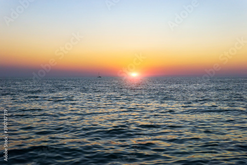 Sailboat silhouetted against a colorful orange sunset sky in the open sea