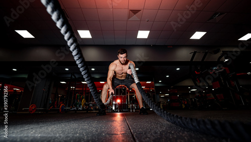 Attractive muscular man working out with heavy ropes. Photo of handsome man. Selective focus from front. Crossfit concept.