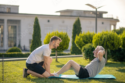Photography Young brown-haired male helping mature grey-haired male with sit ups