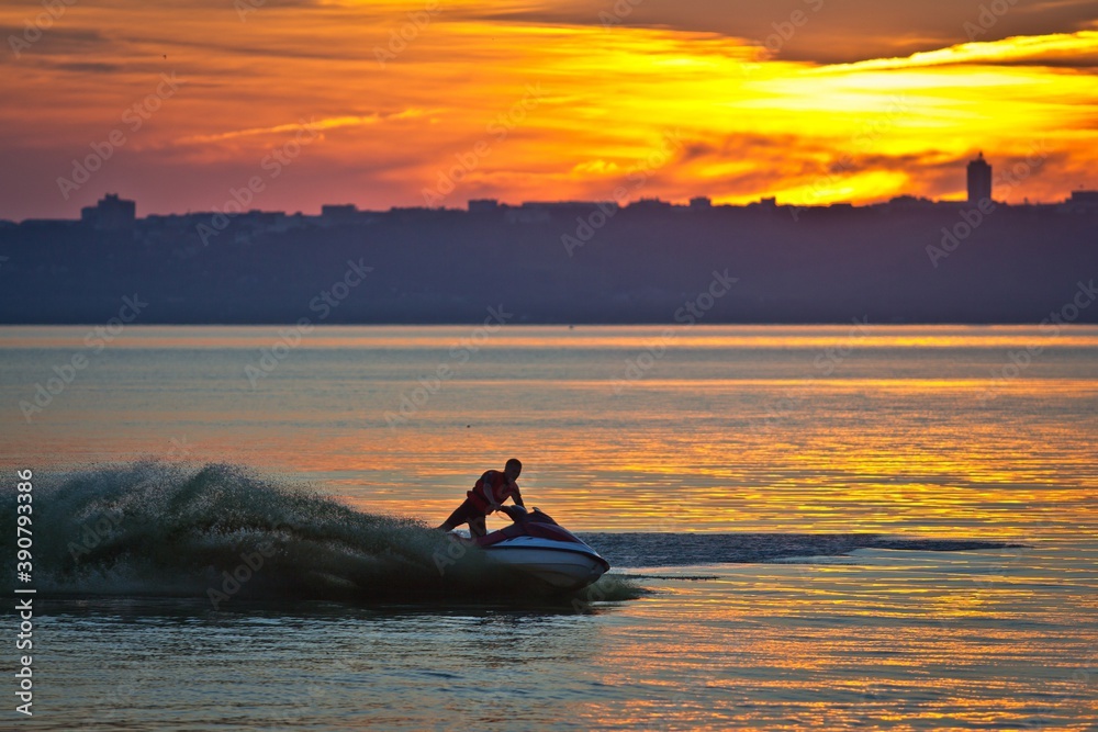 ULYANOVSK, RUSSIA - 20 JULY 2013. A man driving a jet ski on the Volga river at sunset. Blurred cityscape and sky in the background.