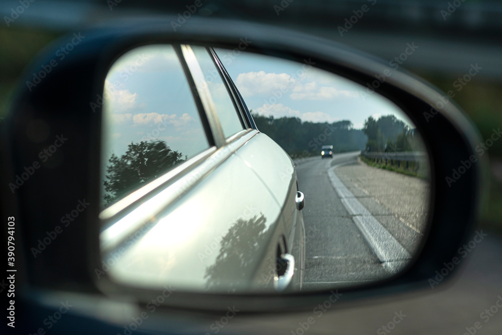 Reflection in the side mirror of a car driving on the highway, visible car in the reflection.