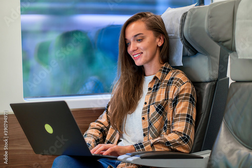 Young casual cute happy smiling smart woman passenger using a laptop for online working, watching video and reading news while traveling by train