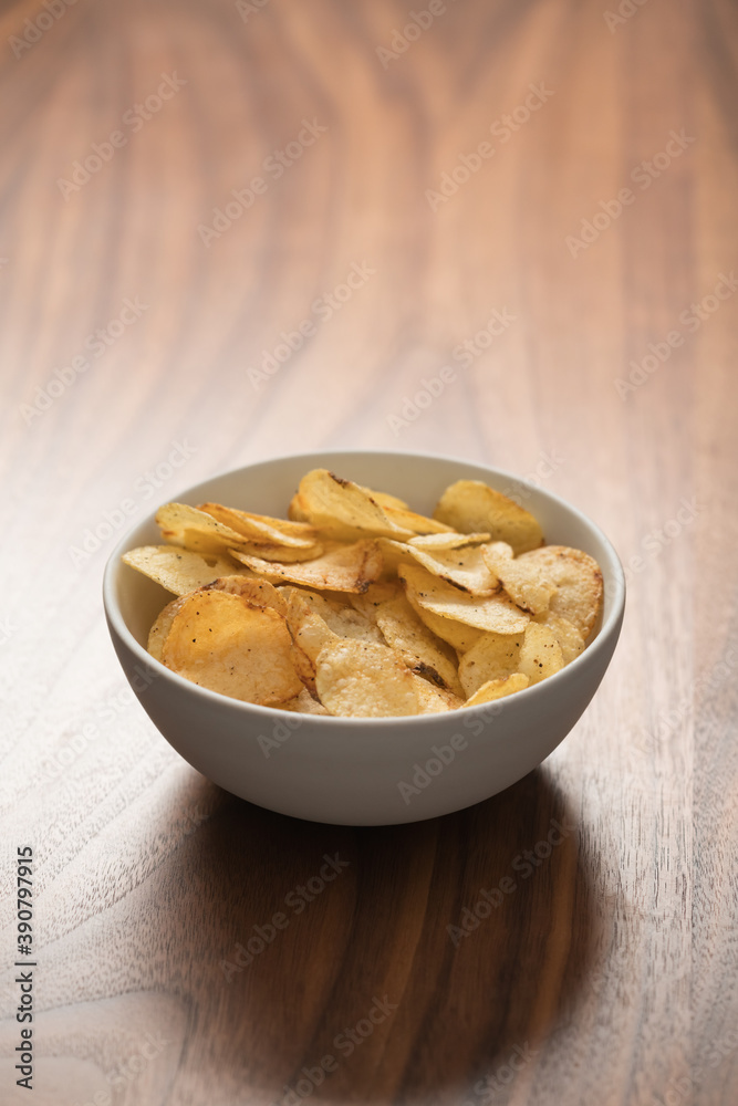 Organic potato chips with black pepper in white ceramic bowl on walnut wood background with copy space