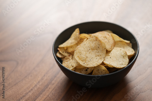 Organic potato chips with black pepper in black ceramic bowl on walnut wood background with copy space