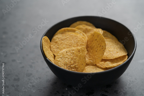 Round nachos in black ceramic bowl on concrete background with copy space