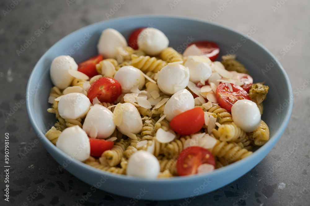 Pesto fusilli with mozzarella balls and tomatoes in blue bowl Pesto fusilli with mozzarella balls and tomatoes in blue bowl