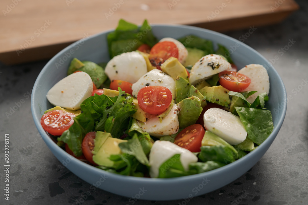 Salad with avocado, cherry tomatoes, romaine and mozzarella in blue bowl on concrete countertop Salad with avocado, cherry tomatoes, romaine and mozzarella in blue bowl on concrete countertop