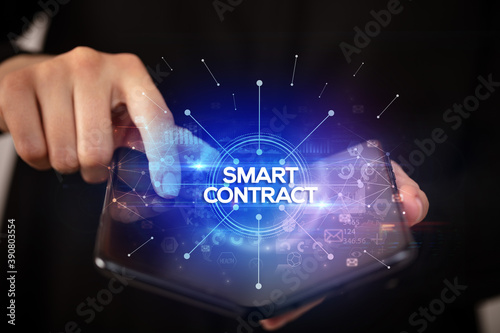 Businessman holding a foldable smartphone with SMART CONTRACT inscription, new business concept